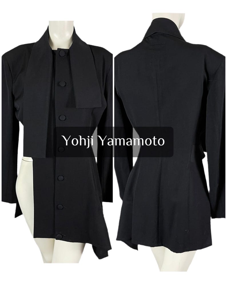 May include: Black Yohji Yamamoto jacket with a unique asymmetrical design. The jacket features a high collar, long sleeves, and a button-up front. The text "Yohji Yamamoto" is displayed on the image.