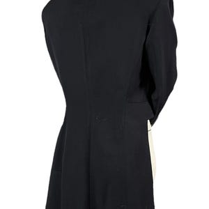 May include: A black blazer with a notched lapel and long sleeves. The back view shows a tailored fit, with a slight flare at the hem. The blazer is made of a smooth, solid fabric.