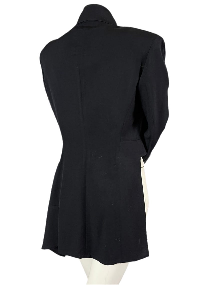 May include: A black blazer with a notched lapel and long sleeves. The back view shows a tailored fit, with a slight flare at the hem. The blazer is made of a smooth, solid fabric.