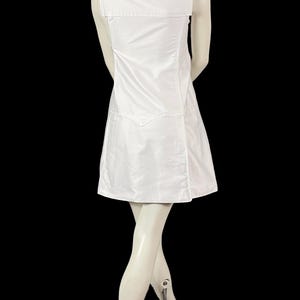 May include: A white dress with a square neckline and wide shoulder straps. The dress has a fitted bodice and a flared skirt. The back of the dress features a large, rectangular panel. The dress is displayed on a mannequin against a black background.