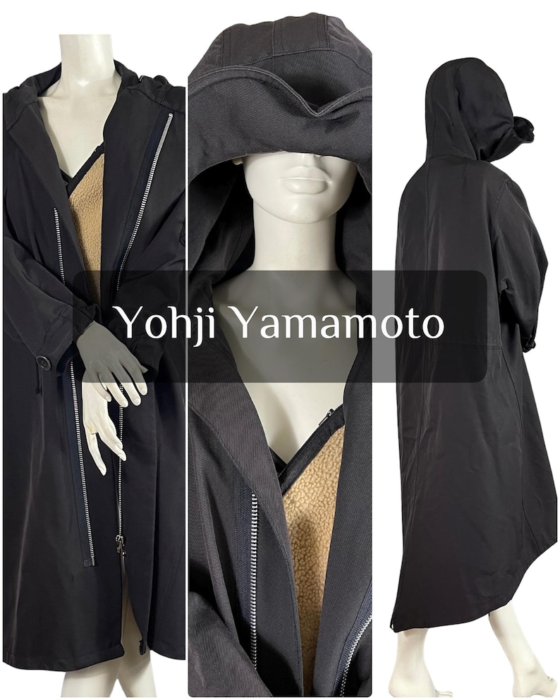 May include: Black long coat with a hood and a zipper closure. The coat has a contrasting tan lining and the text "Yohji Yamamoto" is displayed on the front. The coat is displayed on a mannequin.
