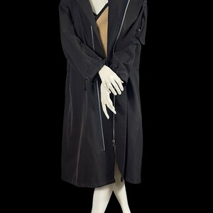 May include: A long black coat with a hood and silver zippers. The coat has a tailored fit and a sleek, modern design. The coat is shown on a mannequin.