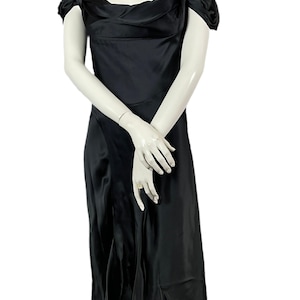 Peut inclure: Une robe noire de longueur midi avec une finition satinée lisse. Le vêtement présente une encolure carrée, des manches courtes tombantes sur les épaules avec des détails froncés, et un corsage ajusté qui se prolonge en une jupe évasée.