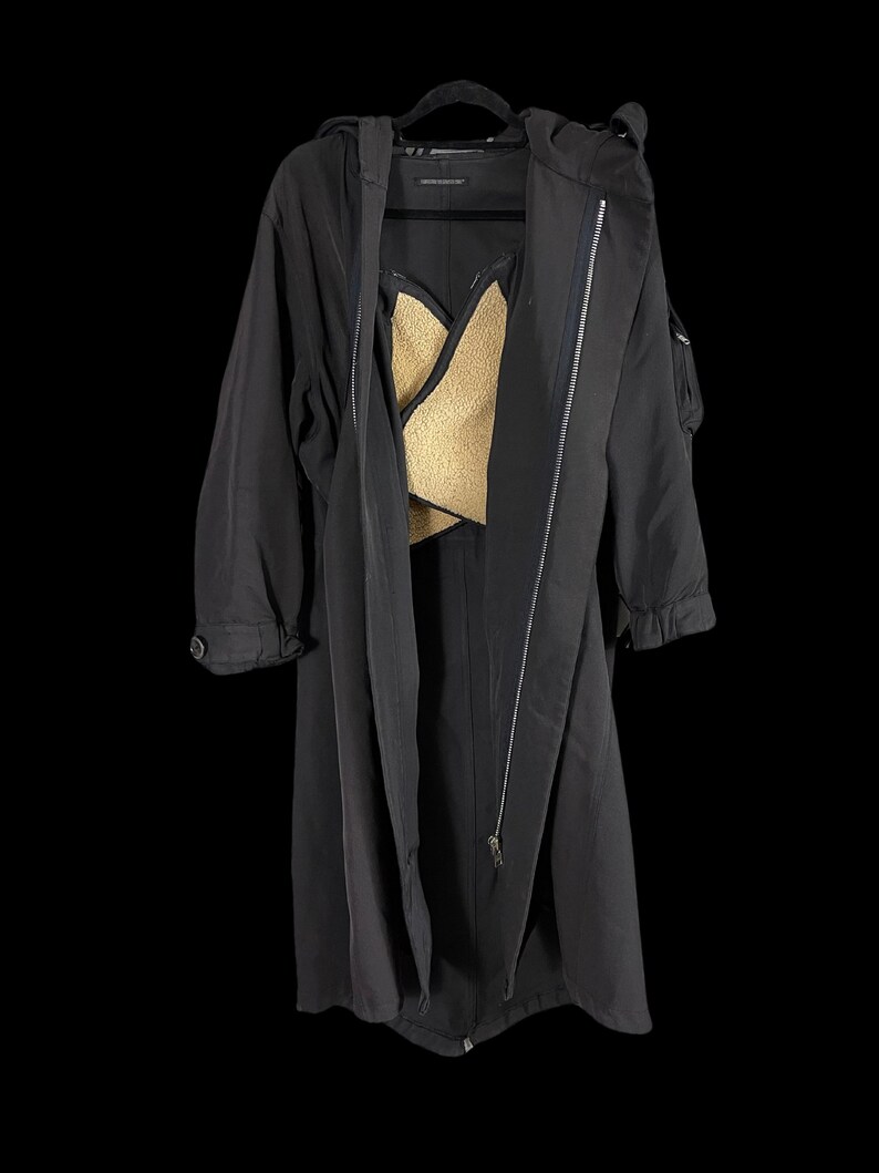 May include: A long black coat with a hood and a zipper closure. The coat has a gold-colored lining visible in the open front. The coat is hanging on a black hanger against a black background.
