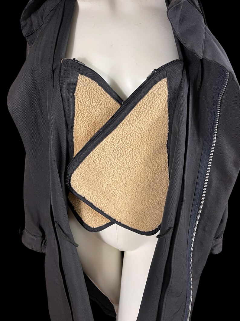May include: A black jacket with a beige, fuzzy lining. The jacket has a zipper closure and a collar. The lining is visible in the chest area. The jacket is displayed on a mannequin against a black background.