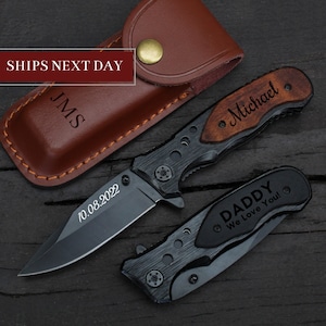 May include: Two personalised pocket knives with black blades and wooden handles. One knife has the text "Michael" engraved on the handle and the other has the text "Daddy We Love You!" engraved on the handle. The knives are on a wooden surface.