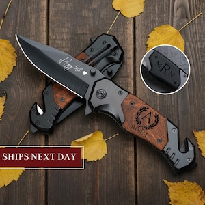 May include: A black folding knife with a wooden handle and a silver blade. The knife has the text "Happy 5th" and "Adam" engraved on it. The knife is lying on a wooden surface with yellow leaves.