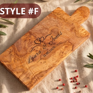May include: Wooden cutting board with a handle, featuring a natural wood grain pattern. The board is engraved with the names "Laura & Jonas" and the date "14.06.2026", along with two heart symbols. The text "STYLE #F" is in the upper left corner.