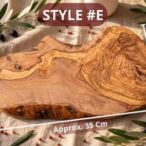 May include: A wooden cutting board, style #E, with a natural edge and a light brown color. The board is approximately 14 inches long and 8-12 inches wide. Olive branches and berries surround the board.