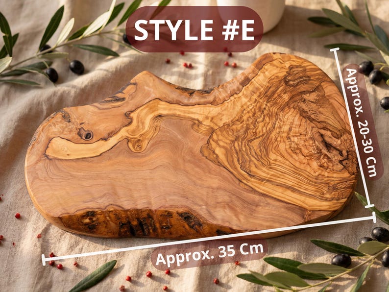 May include: A wooden cutting board, style #E, with a natural edge and a light brown color. The board is approximately 14 inches long and 8-12 inches wide. Olive branches and berries surround the board.