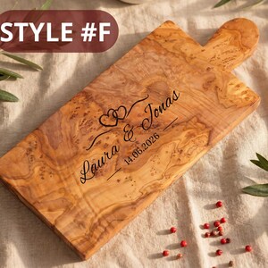 May include: Wooden cutting board with a handle, featuring a natural wood grain pattern. The board is engraved with the names "Laura & Jonas" and the date "14.06.2026", along with two heart symbols. The text "STYLE #F" is in the upper left corner.