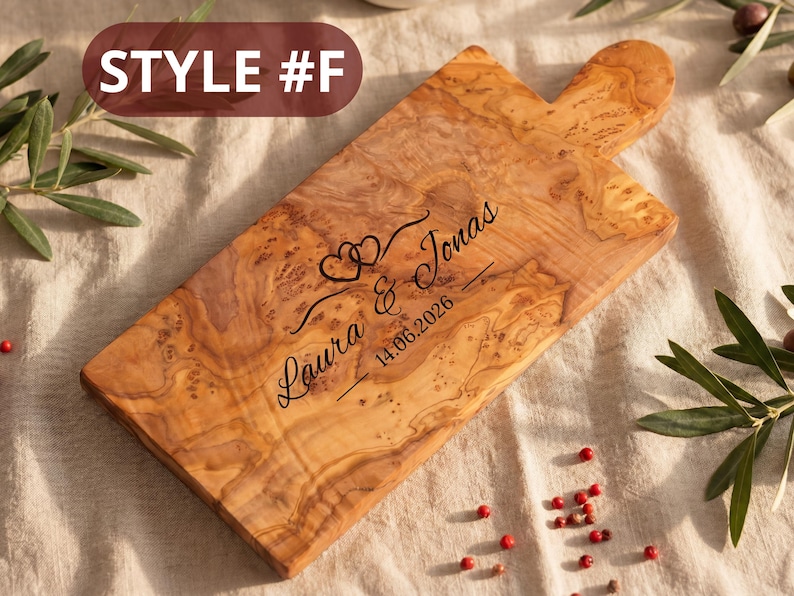 May include: Wooden cutting board with a handle, featuring a natural wood grain pattern. The board is engraved with the names "Laura & Jonas" and the date "14.06.2026", along with two heart symbols. The text "STYLE #F" is in the upper left corner.
