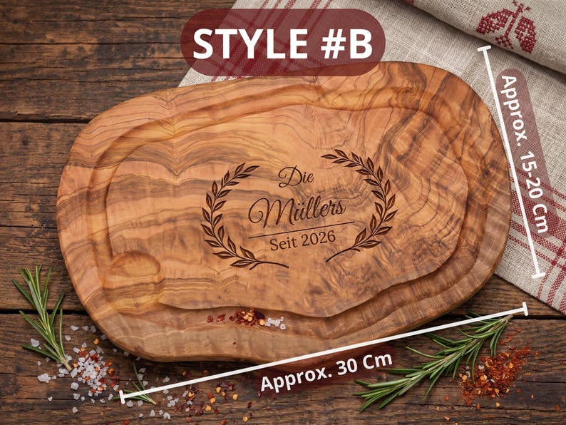 May include: Oval wooden cutting board, approximately 30 cm long and 15-20 cm wide, with a carved groove. The board features engraved text and a laurel wreath design. The text reads "Die M&uuml;llers Seit 2026".