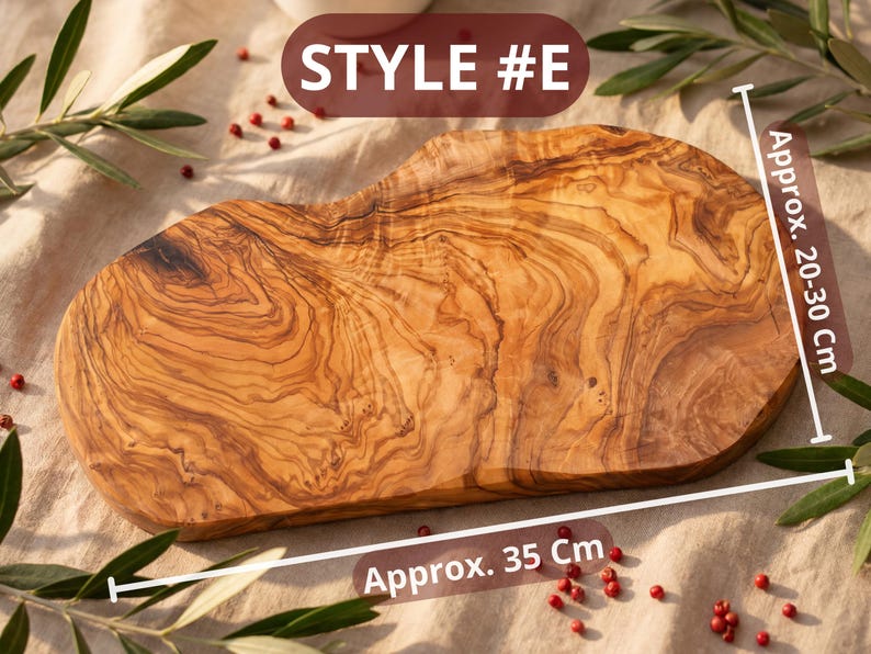May include: A wooden cutting board with a natural wood grain pattern. The board is approximately 14 inches long and 8-12 inches wide. The text "STYLE #E" is displayed on the top. The board is surrounded by olive branches and red peppercorns.