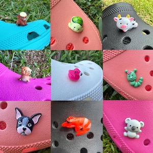 May include: A selection of shoe charms in various designs: a brown bull, a green turtle, a black and white cow, a tan cat, a pink flamingo, a green caterpillar, a black and white dog, an orange shrimp, and a white koala bear. These charms are for shoe decoration.