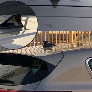 May include: A close-up of a black shark fin antenna on a silver car. The antenna is mounted on the roof of the car.