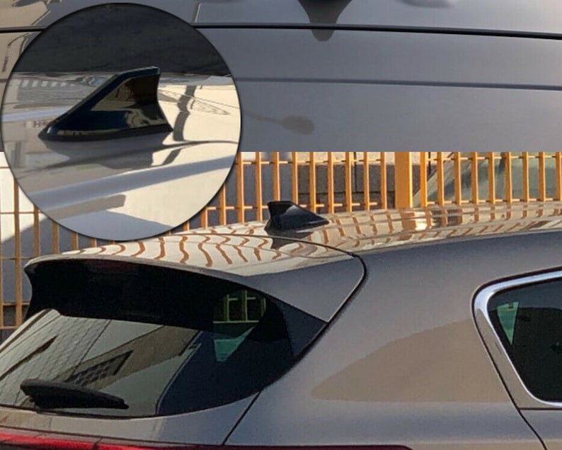 May include: A close-up of a black shark fin antenna on a silver car. The antenna is mounted on the roof of the car.