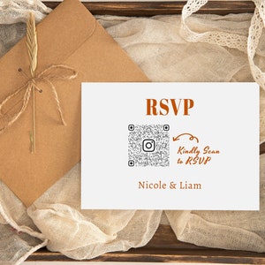 Peut inclure: Une carte blanche avec le mot "RSVP" en texte brun. Un code QR noir et blanc est sur la carte avec une flèche pointant vers le texte "Kindly Scan to RSVP" en texte brun. Le texte "Nicole & Liam" est sous le code QR en texte brun. La carte est sur une surface en bois brun avec une enveloppe brune et un tissu blanc.