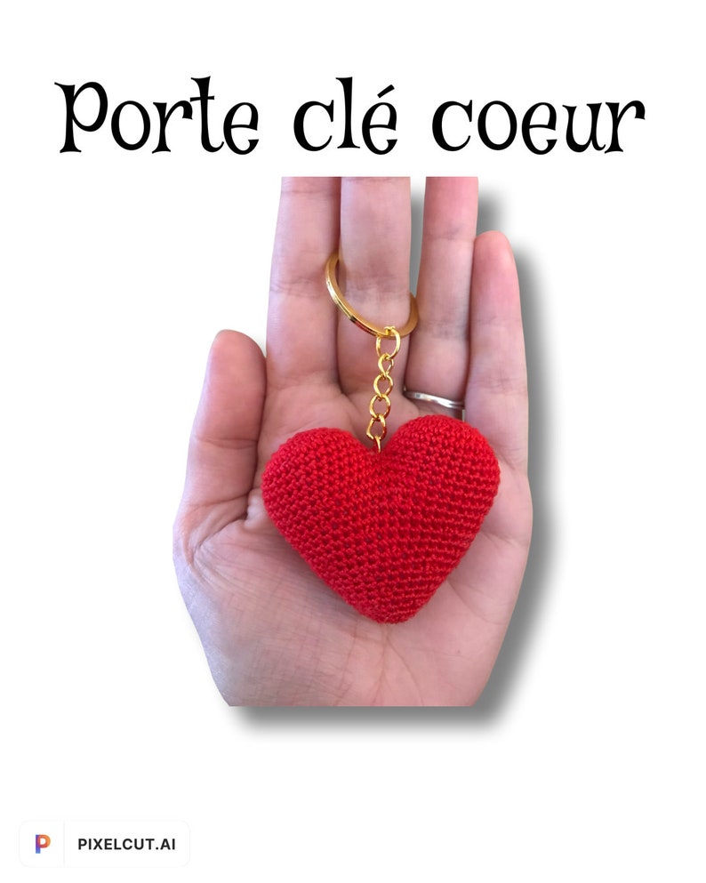 Puede incluir: Llavero de coraz&oacute;n rojo tejido a crochet con una cadena y un anillo dorados. El llavero se sostiene en una mano.