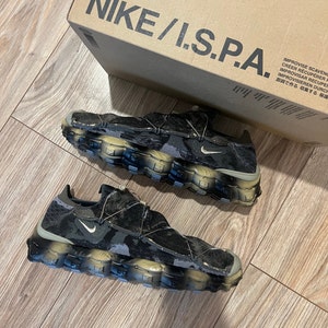 May include: A pair of black and grey Nike I.S.P.A. trainers with a camouflage pattern. The trainers have a chunky, multi-layered sole.