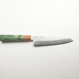 Puede incluir: Cuchillo de chef de estilo japon&eacute;s con una hoja plateada texturizada y un mango en tonos verdes, marrones y beige. Dise&ntilde;ado para cortar con precisi&oacute;n y preparar alimentos.