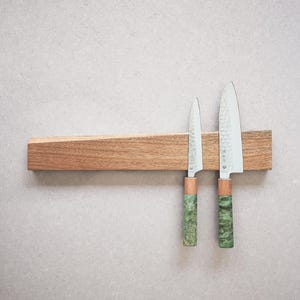 May include: A horizontal wooden magnetic knife strip holding two kitchen knives. The knives feature silver blades with a hammered texture and green marbled handles with a light wood accent near the bolster, positioned vertically on the strip.