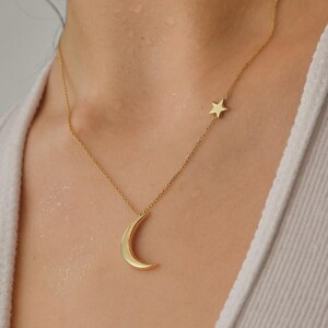 Pu&ograve; includere: Una collana d'oro con un ciondolo a forma di luna crescente e un piccolo ciondolo a forma di stella.