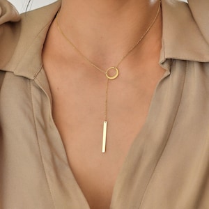 May include: A gold necklace with a circle pendant and a long, thin bar pendant.