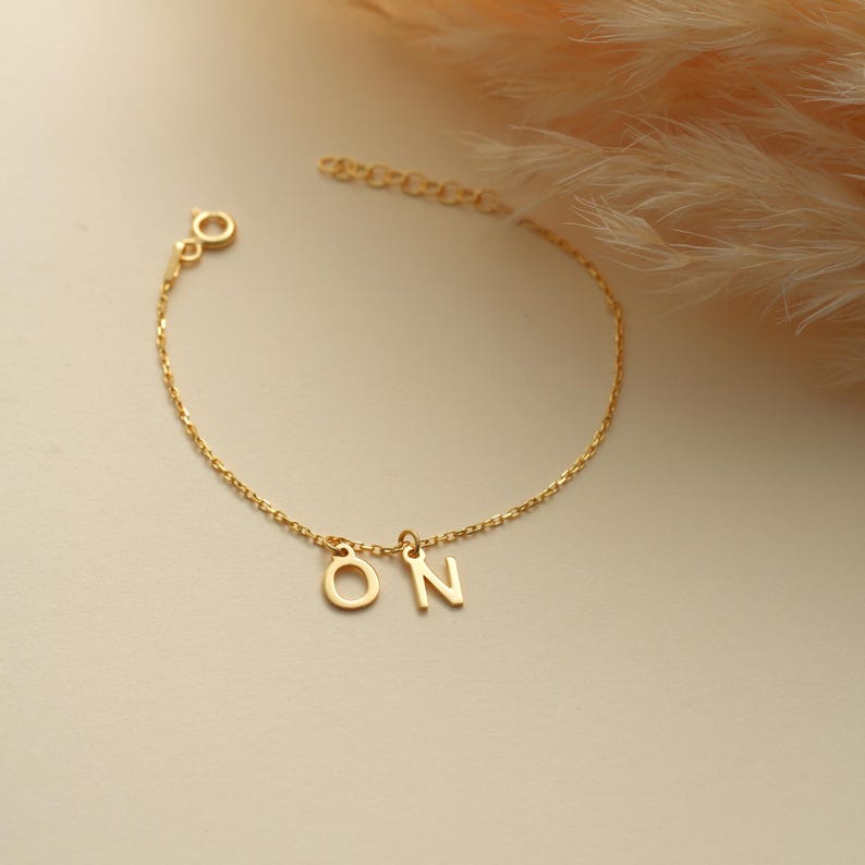 K&ouml;nnte beinhalten: Ein goldenes Kettenarmband mit den Buchstaben "ON", die daran h&auml;ngen.