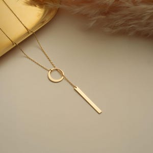 May include: A gold necklace with a circle pendant and a long, thin bar pendant.