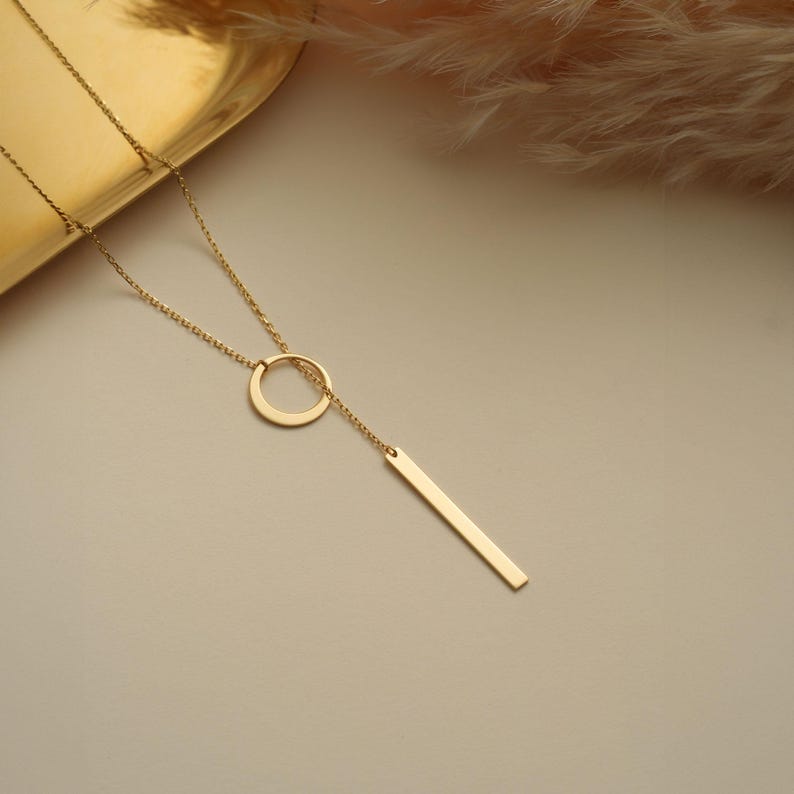 May include: A gold necklace with a circle pendant and a long, thin bar pendant.