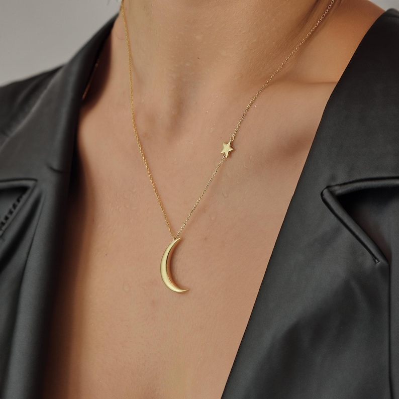 Pu&ograve; includere: Una collana d'oro con un ciondolo a forma di luna crescente e un piccolo ciondolo a forma di stella.