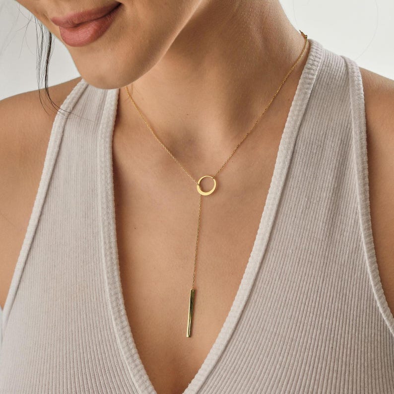 May include: A gold necklace with a circle pendant and a long, thin bar hanging from the bottom.