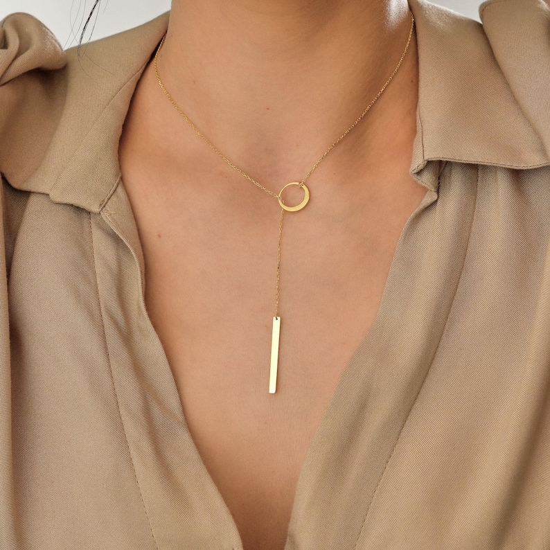 May include: A gold necklace with a circle pendant and a long, thin bar pendant.