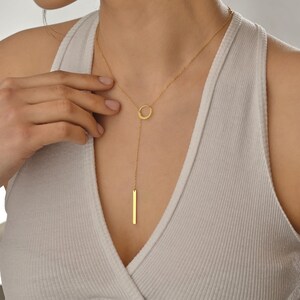 May include: A gold necklace with a circle pendant and a long, thin bar pendant hanging from it.