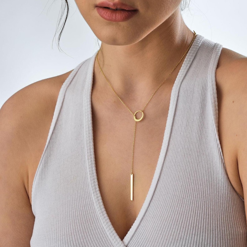 May include: A gold-toned necklace with a circle pendant and a long, thin bar hanging from it.