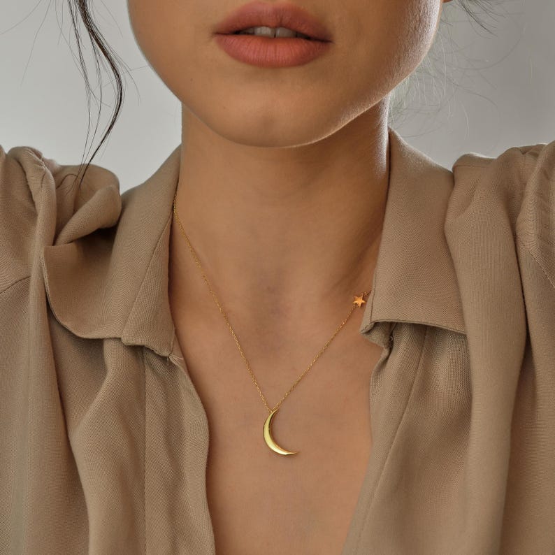Pu&ograve; includere: Una collana d'oro con un ciondolo a forma di luna crescente e un piccolo ciondolo a forma di stella.