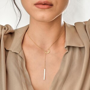 May include: A gold necklace with a circle pendant and a long, thin bar pendant hanging from it.