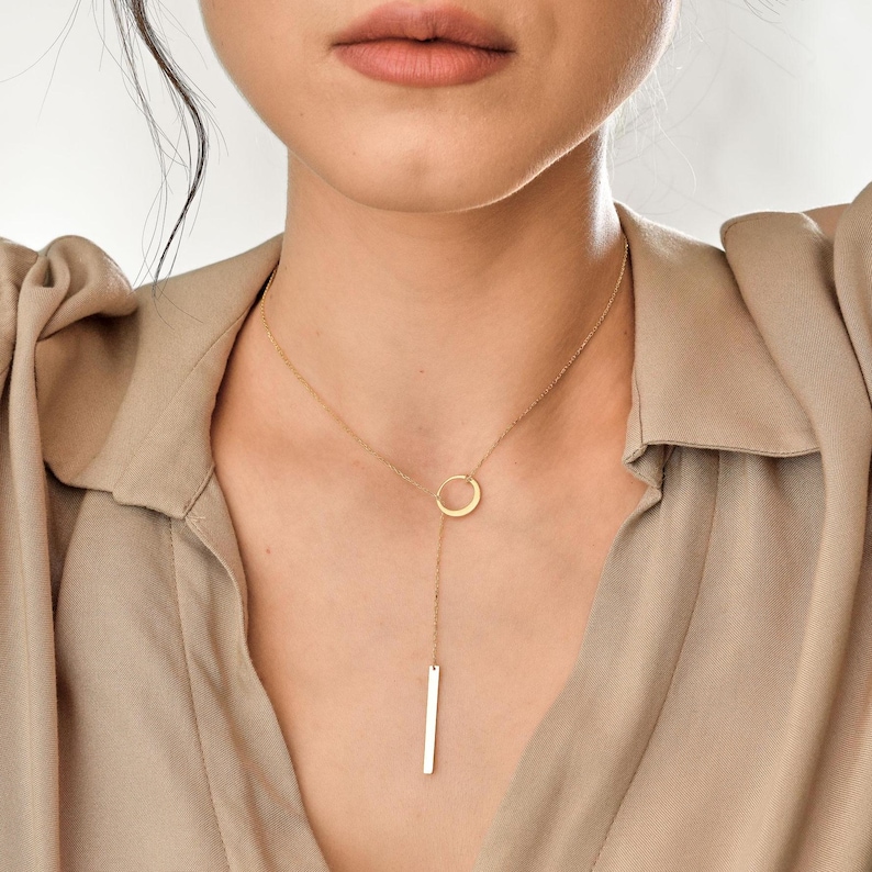 May include: A gold necklace with a circle pendant and a long, thin bar pendant hanging from it.