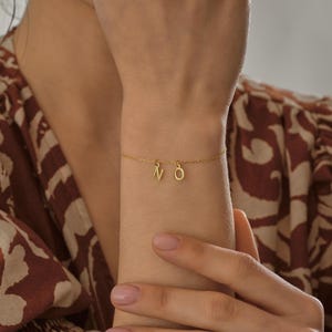 K&ouml;nnte beinhalten: Ein goldenes Kettenarmband mit den Buchstaben "N" und "O", die daran h&auml;ngen.