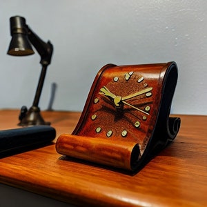 May include: A wooden clock with a scroll design and gold-colored hands. The clock face is brown with gold-colored accents.