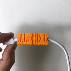 以下が含まれることがあります： オレンジ色のプラスチック製のケーブルオーガナイザーで、"NAME HERE"という文字が印刷されています。