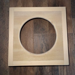 Op de afbeelding: Een vierkant houten frame met een ronde uitsparing in het midden. Het frame is gemaakt van licht hout en heeft een natuurlijke afwerking.