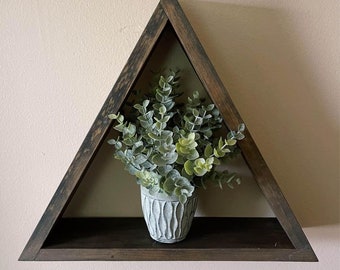 Puede incluir: Una estantería triangular de madera con una mancha marrón oscura. La estantería tiene una pequeña planta en maceta con hojas verdes.