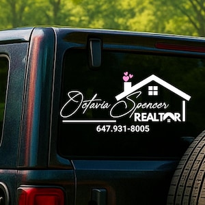 May include: A white decal on a black vehicle window featuring the name "Octavia Spencer" in cursive, a house graphic, and the word "REALTOR." The phone number 647.931-8005 is also displayed.