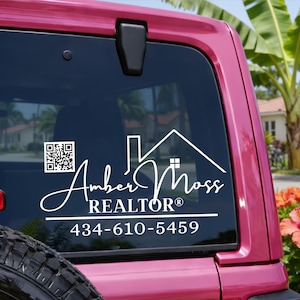 May include: White decal on a pink vehicle window. The decal features the name "Amber Moss REALTOR®" with a house graphic and a QR code. The phone number 434-610-5459 is also included.