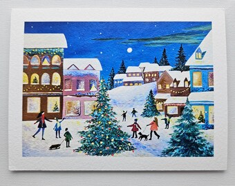 以下が含まれることがあります： 夜の雪景色を描いたアートプリント。 窓が照らされた建物、装飾されたクリスマスツリー、冬の天候を楽しむ人々が特徴です。 空は深い青色で、満月が描かれています。