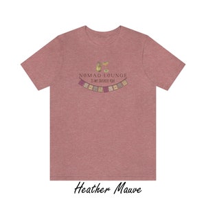K&ouml;nnte beinhalten: Heather-mauvefarbenes T-Shirt mit einem Grafikdruck eines Cocktails und dem Text "Nomad Lounge is my favorite ride" sowie einer Girlande aus bunten Flaggen.