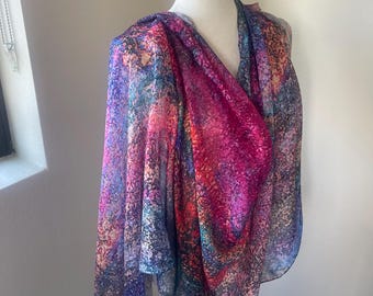May include: A colorful abstract print scarf in shades of pink, blue, and green. The scarf is draped over a white mannequin.
