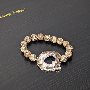 May include: A gold and brown agate stone bracelet with a silver agate charm. The charm has a large hole in the center.